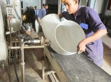 Worker handling a circular metal component at a forming machine
